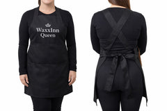 Black apron with 'WaxxInn Queen' text worn by a person on a white background